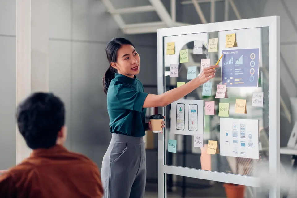 Professional business consultation scene showing a team member presenting project plans, analytics, and digital transformation ideas on a collaborative planning board. The visual reflects the step-by-step process of applying for the PSG E-commerce Grant in Singapore, highlighting strategic planning, digital adoption, and business growth initiatives supported by RHAD.